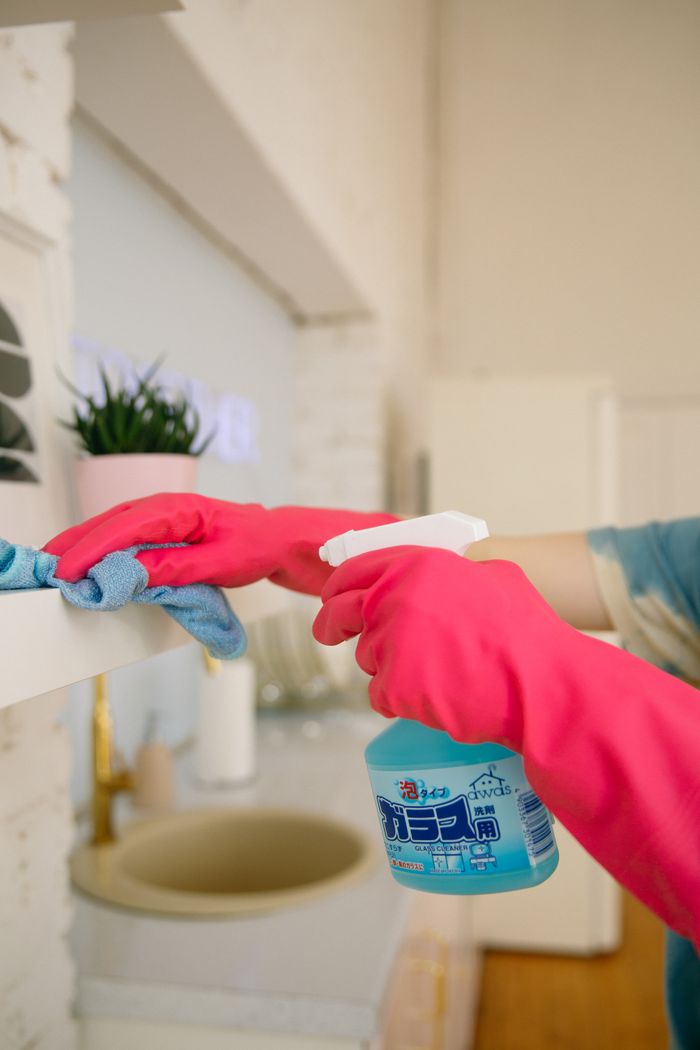 An individual cleans a kitchen shelf with a spray bottle and cloth, helping maintain hygiene and a spotless finish.